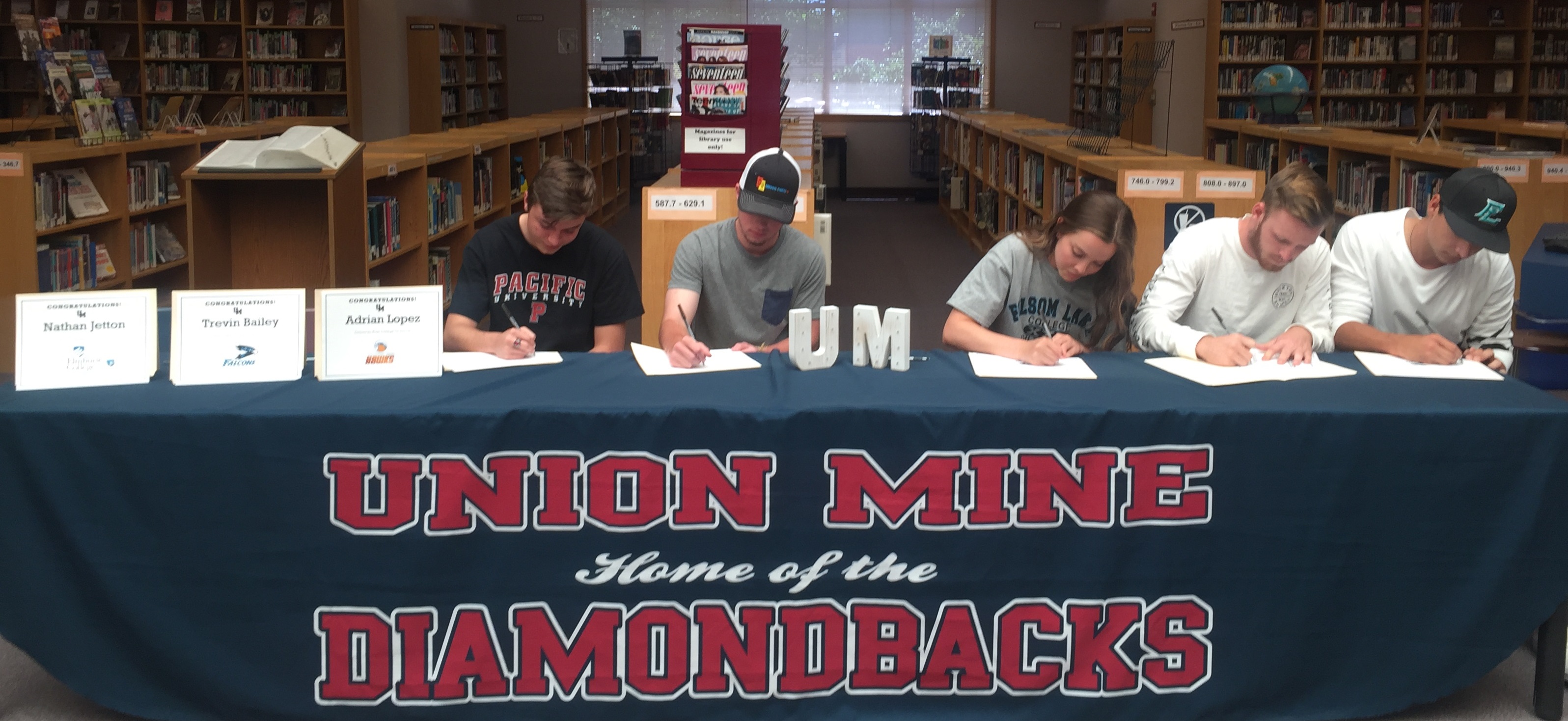 Athletes signing papers at a table with their certificates